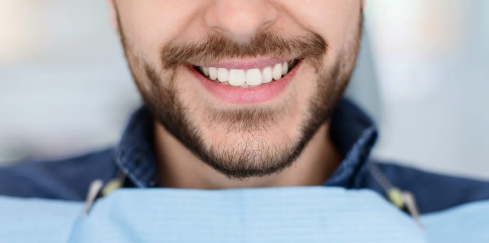 Closeup of man dental clinic patient white healthy smile, unrecognizable bearded man with napkin on his chest showing his beautiful smile, showing result of treatment at modern dentistry, cropped
