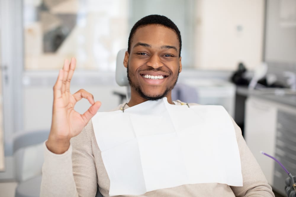 Confident patient smiling after treatment – Dental implants in Nashville Man sitting in a dental chair giving an OK sign and smiling confidently after receiving professional care – Dental implants in Nashville