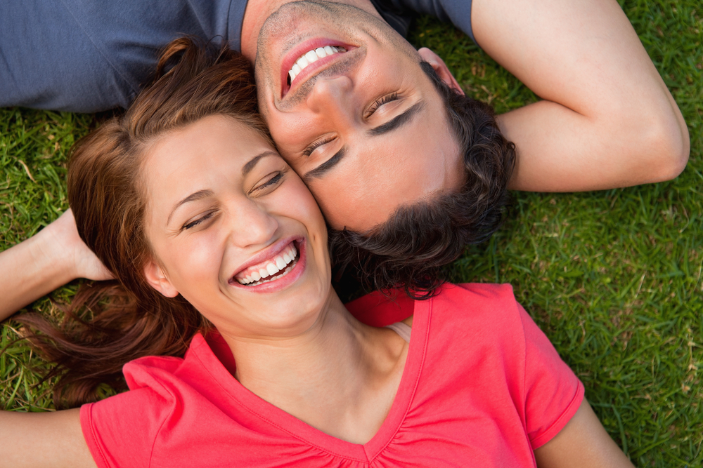 Smiling couple relaxing on the grass, showcasing healthy, confident smiles that reflect excellent dental care - Berry Hill Dentist