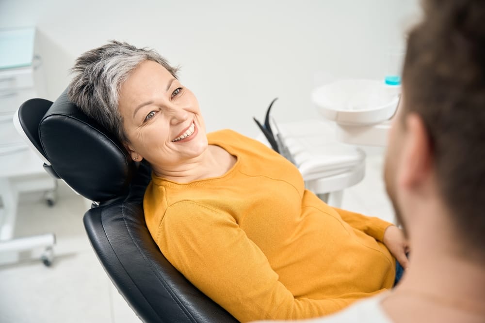 Smiling woman at the dentist’s office – Dental implants in Nashville Older woman reclining in a dental chair, smiling and speaking with her dentist during a consultation – Dental implants in Nashville